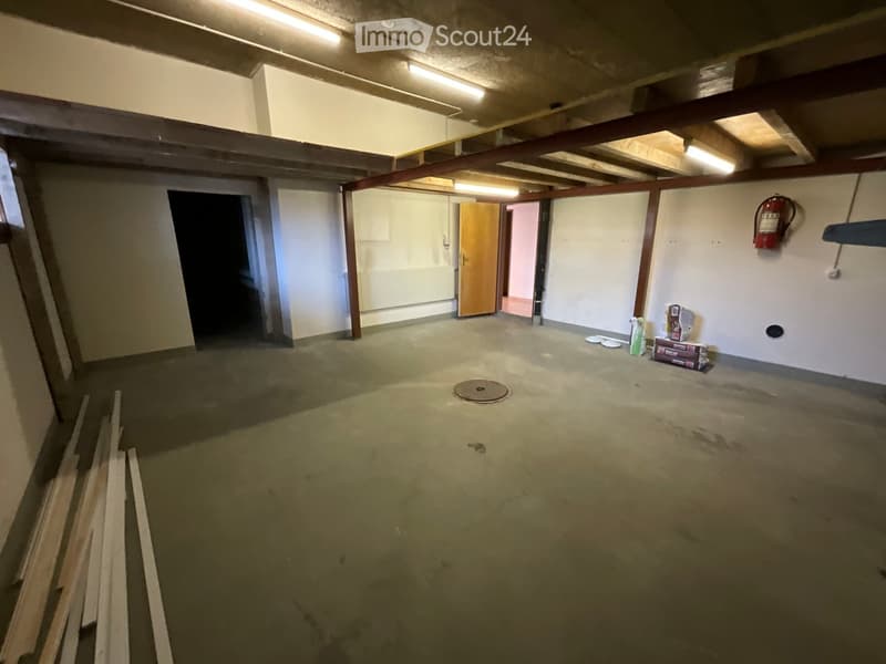 Concrete floor, wooden beams, white walls, open doorway, storage boxes, fire extinguisher