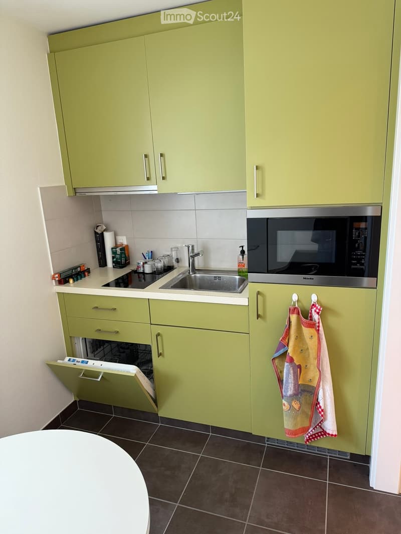 Lime green cabinetry, stainless steel sink, dishwasher, induction cooktop, microwave, tiled flooring, white countertop