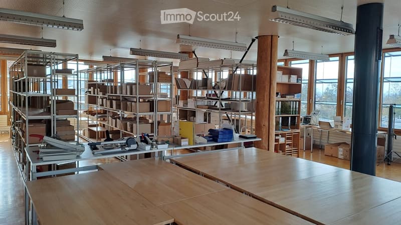 Open room with a wooden floor and multiple wooden tables. Many storage boxes on metal shelves. There are also shelves with some office materials.