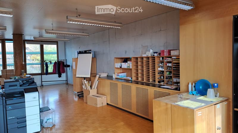 large empty office room with a wooden floor, shelves, desk, printer and whiteboard, and a few clothes hanging on a clothes rack.