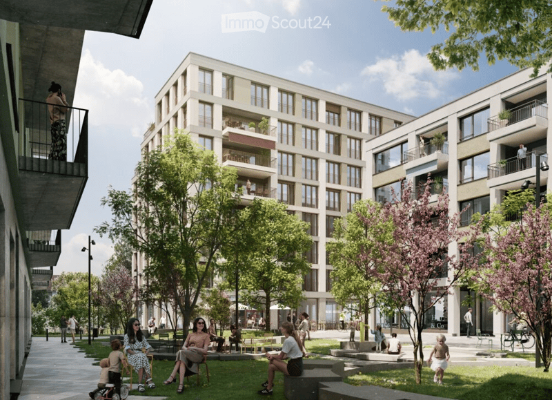 Modern apartment complex with multiple buildings, balcony on the left building, people sitting on the lawn in front, street with trees and people, one person on the balcony