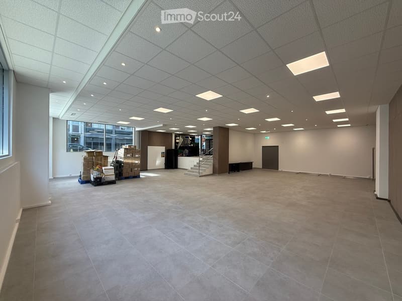 large open space, tiled floor, white walls, ceiling with recessed lighting, large windows, staircase, storage boxes