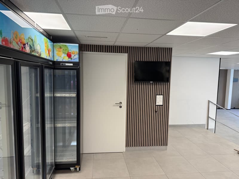 Empty room with white door, tiled floor, two refrigerators, mounted TV, and striped wall