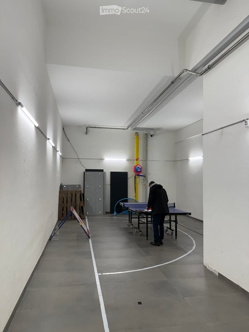 Corridor with tables, a wooden sign, storage boxes, and fluorescent ceiling lights.