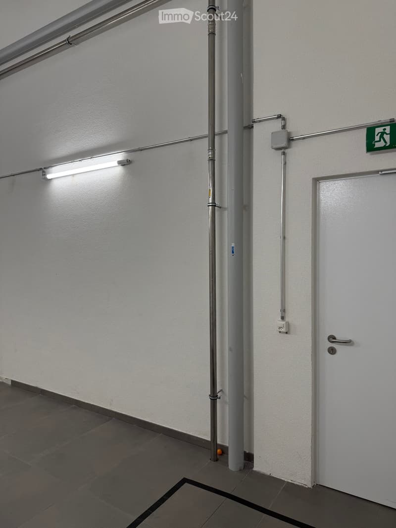 white walls, gray tile floor, a door, pipes and electrical outlets mounted on the wall