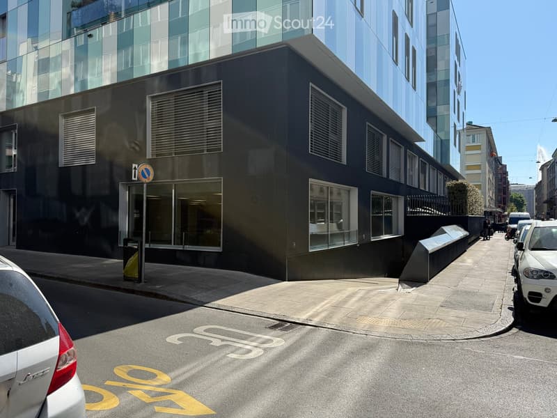 Modern building with glass windows, black exterior, located on a street with parked cars