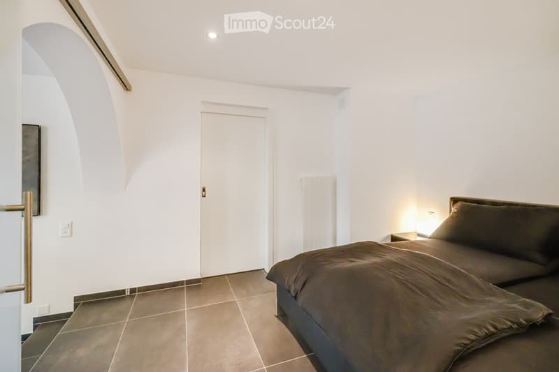bedroom with a large bed, white walls, wooden floor, a nightstand, and a lamp