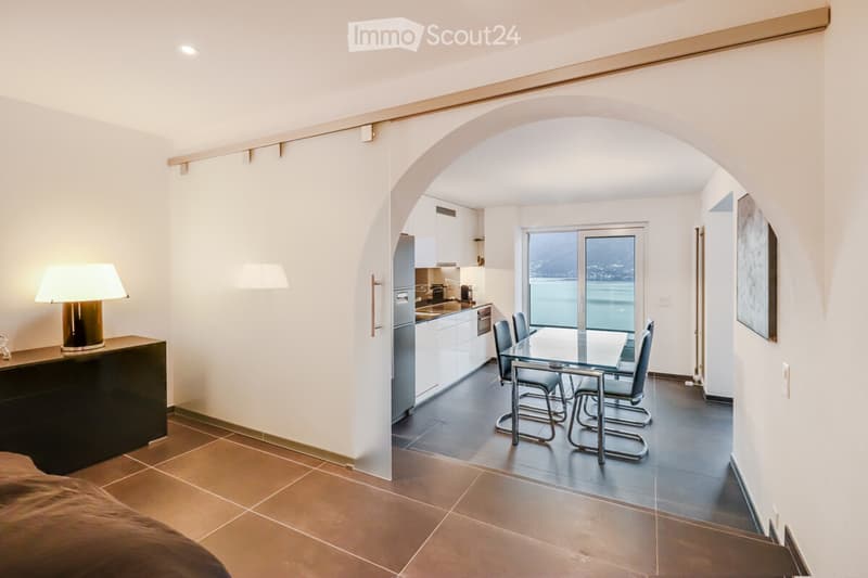 minimalist living room with a dining area, wooden floors, kitchen, glass door leading to balcony with lake view