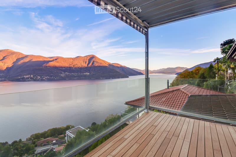 Outdoor balcony with a glass railing, wooden floor, view of lake and mountains