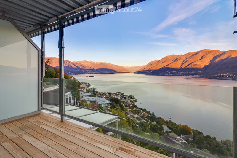 Outdoor balcony with glass railing, wooden floor, scenic mountain and lake view.
