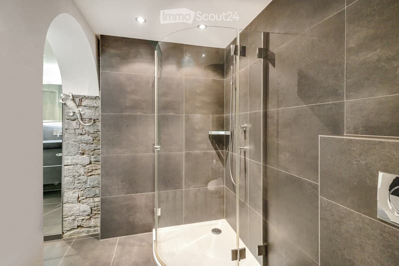 Bathroom with a glass shower, tiled walls, small alcove with a mirror, stone wall, no window