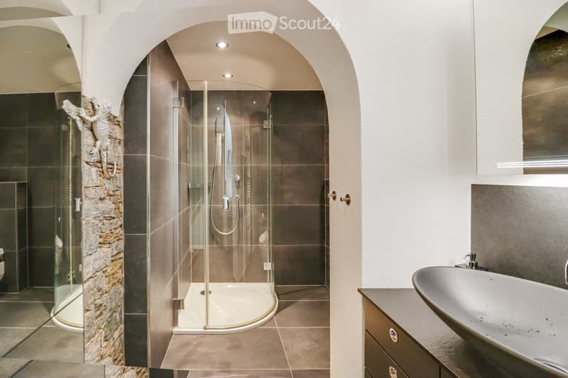 glass walk-in shower, stone wall, vanity sink, wooden cabinets, curved archway