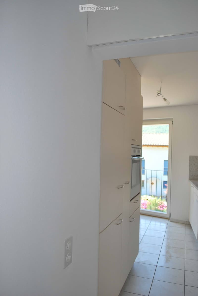 Empty kitchen, tiled floor, built-in oven, white cupboards, balcony with a view of a building and garden
