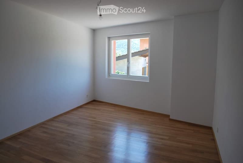 An empty room with white walls, wooden floor, a window, and a light fixture.