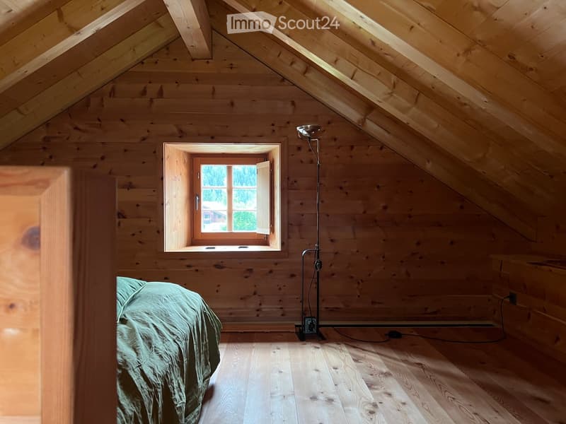 room with wooden walls and floor, a window, bed with green sheets, floor lamp, wooden headboard