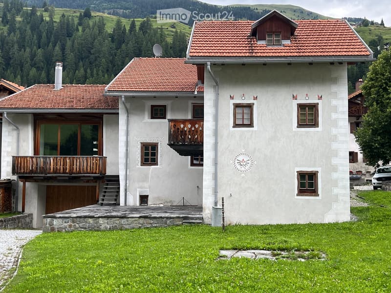 White house with red roof, wooden balcony on second floor, satellite dish, chimney, grassy lawn in front, stone walkway
