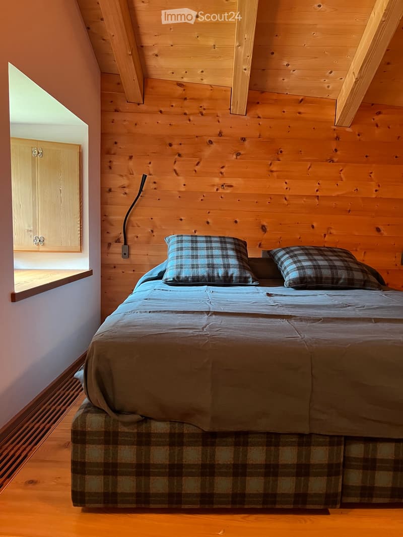large bed with plaid cover, plaid pillow, wall is wooden with wooden ceiling beams