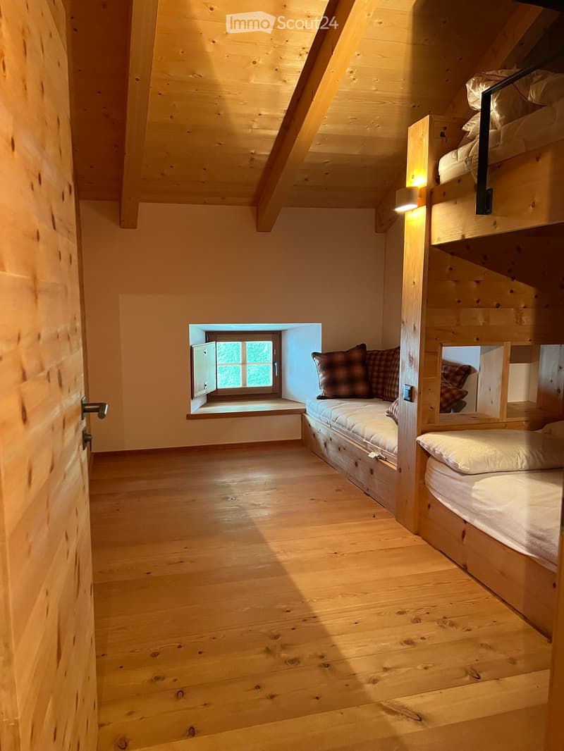 room with wooden floor, two wooden bunk beds, a bench window seat with cushions, a wall lamp