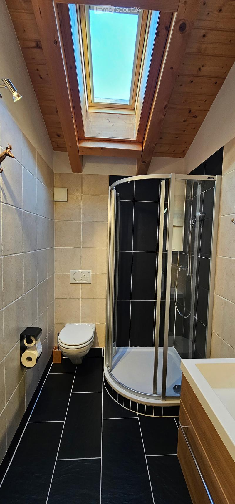 Bathroom with modern shower, toilet, wooden ceiling, skylight, black tile floor, beige tile wall