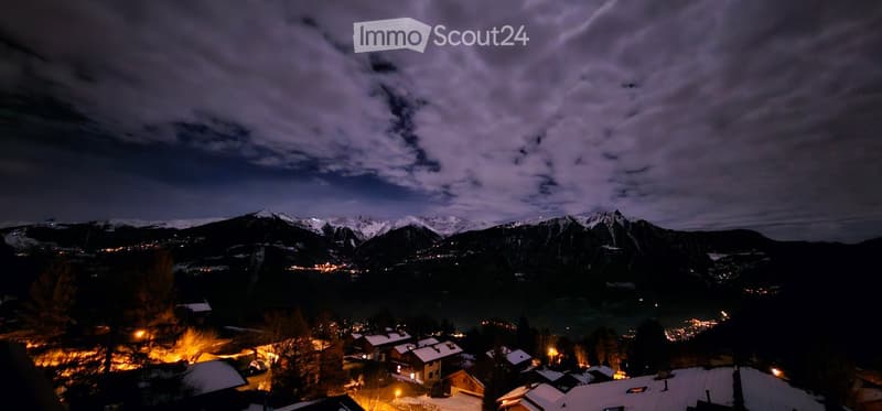 Night view of a town in the Alps with mountains in the background and lights on the buildings.