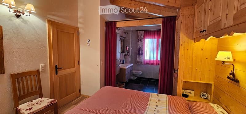 Double bed, wooden chair with cushion, wooden cabinet, toilet room with sink, bathtub, and toilet, lamp, and lampshade