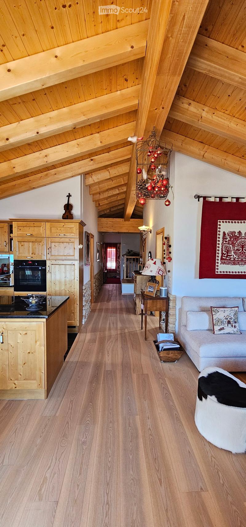 Exposed wooden beams, hardwood floors, wooden kitchen cabinets, black countertop, modern lighting, cozy couch, decorative items