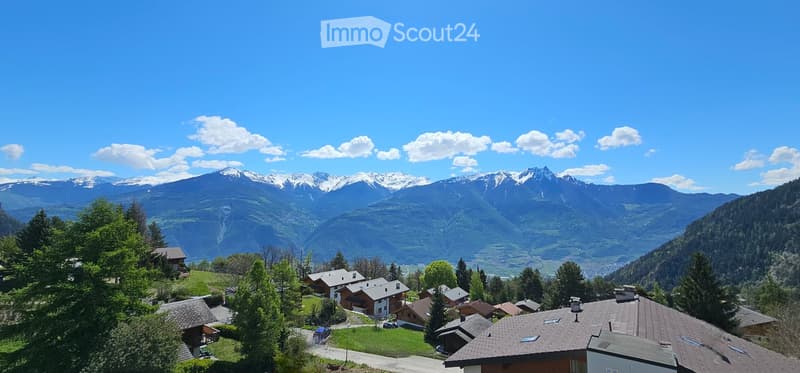 Group of wooden houses set on slopes of mountains. Landscape covered by greenery and trees. Road leading to the houses.