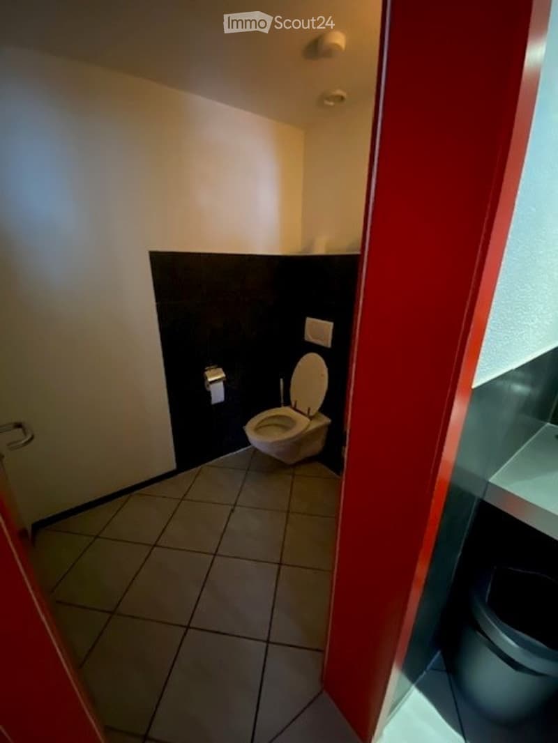 small toilet room with white and red wall, tiled floor, and black bottom wall