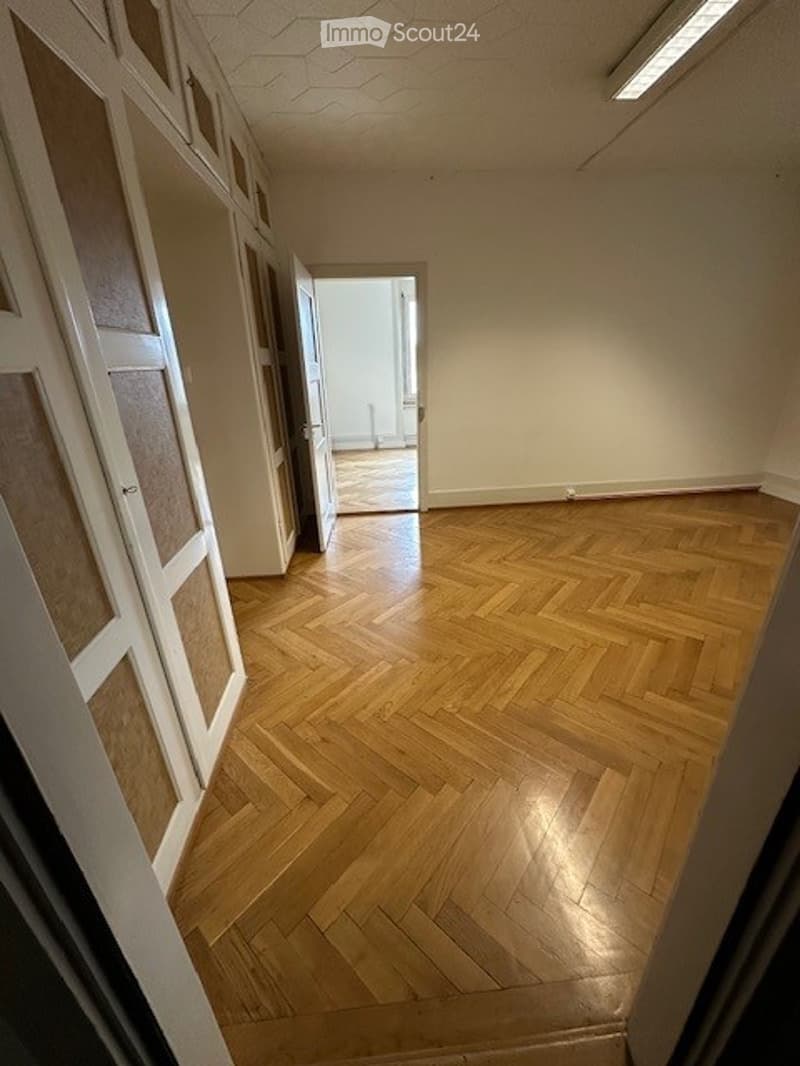 Empty room with parquet floors, white walls, open door leading to another room, large wardrobes