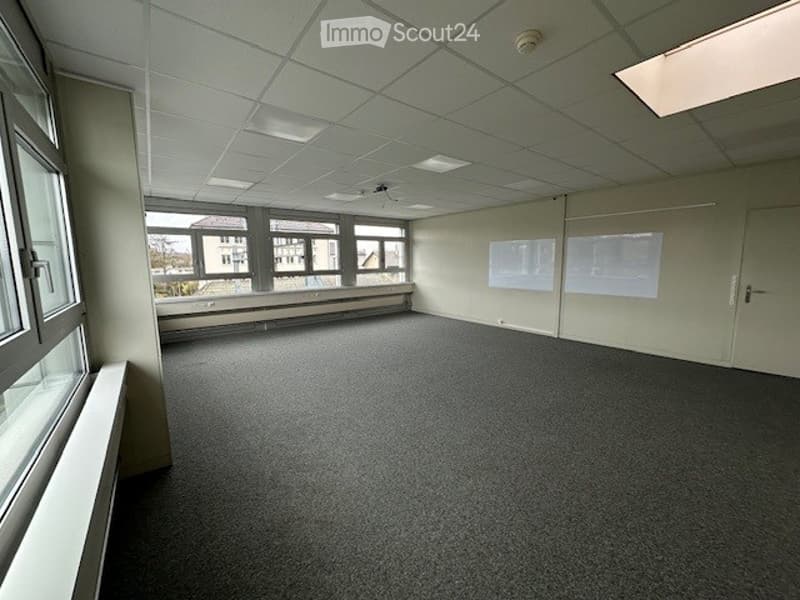 Empty room, carpeted floor, white walls, large windows, two doors, radiators, and a window seat.