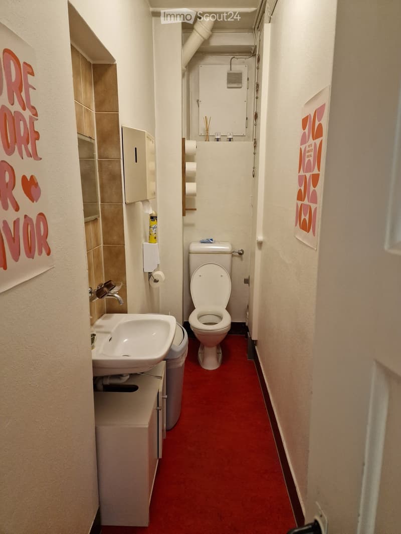 Toilet, sink, white cabinet, red floor, wall mounted tissue dispenser, pink graffiti on wall
