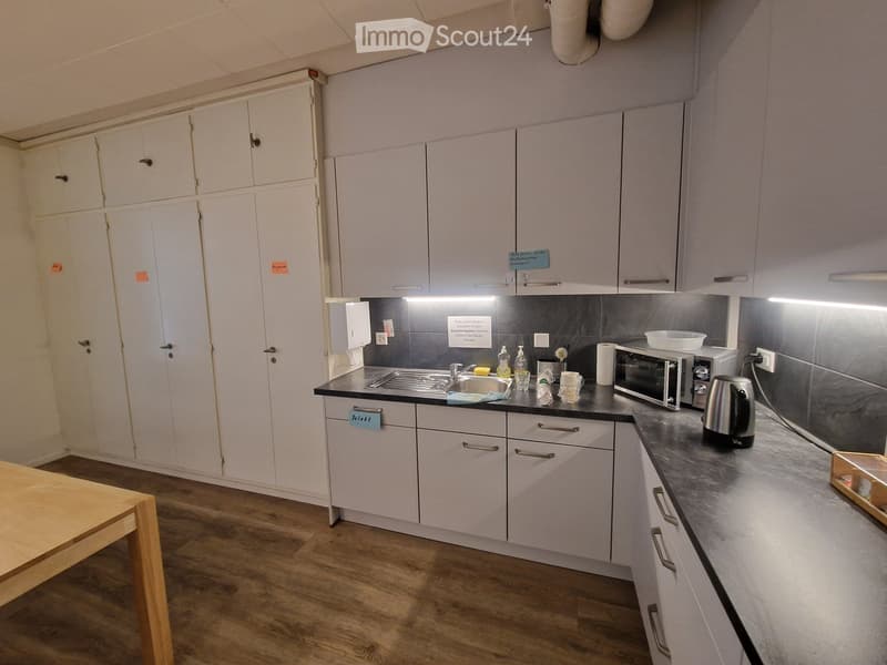Kitchen with wooden floor, white cabinets, countertop, sink, cabinets, microwave, tea kettle, and countertop lighting.