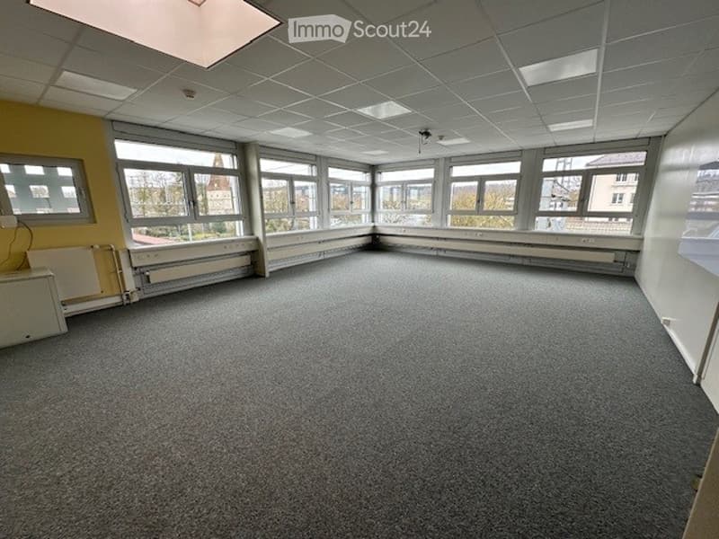 Empty room with large windows, yellow wall, gray carpet, radiator, ceiling lights, power outlet