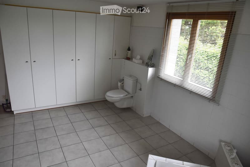 a bathroom with tiled floor, white walls, built-in cabinets, a toilet, a mirror, and a window with blinds