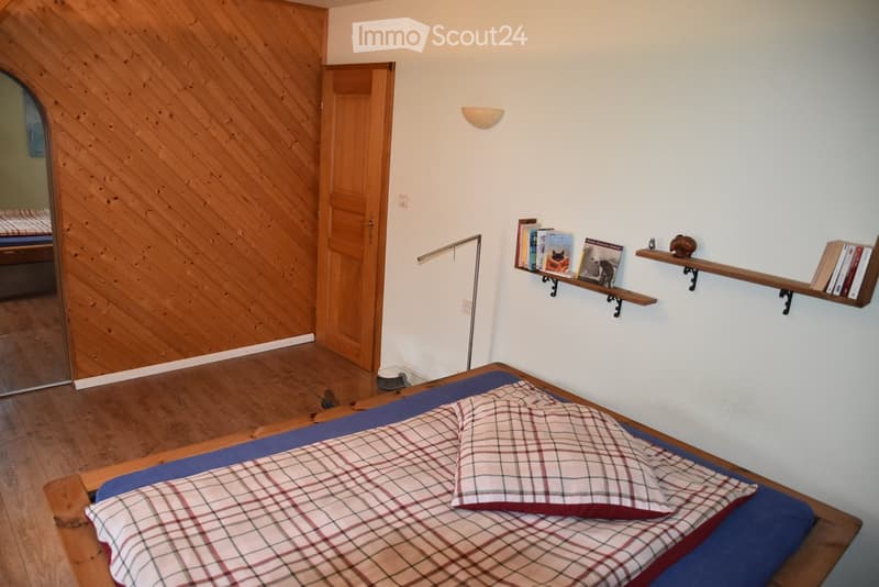 A bedroom with wooden wall, wooden bed, plaid sheet, pillow, lamps, books on the wall