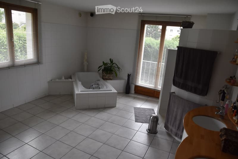 White tile flooring, white bathtub, white walls, potted plant, two sinks, window with blinds