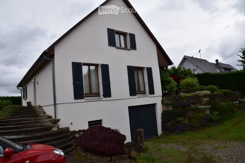 two story house, white walls, black shutters, black garage door, driveway, steps at entrance, bushes and plants