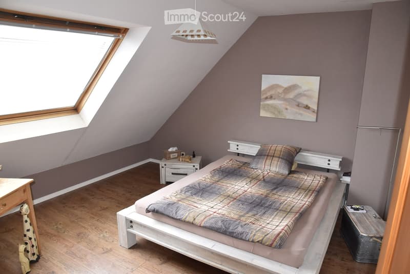 Bedroom with bed, nightstand, painting on the wall, desk, and a skylight window.