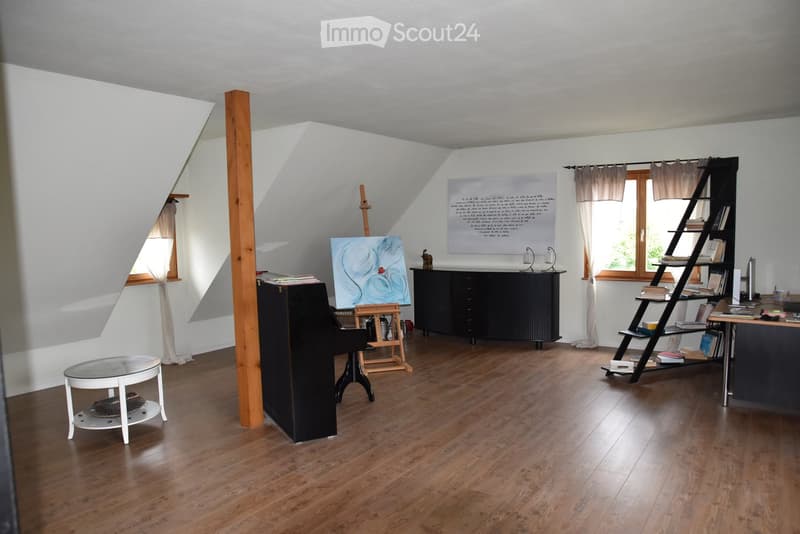 wooden floor, white wall, desk, piano, shelves with books, windows, painting stand