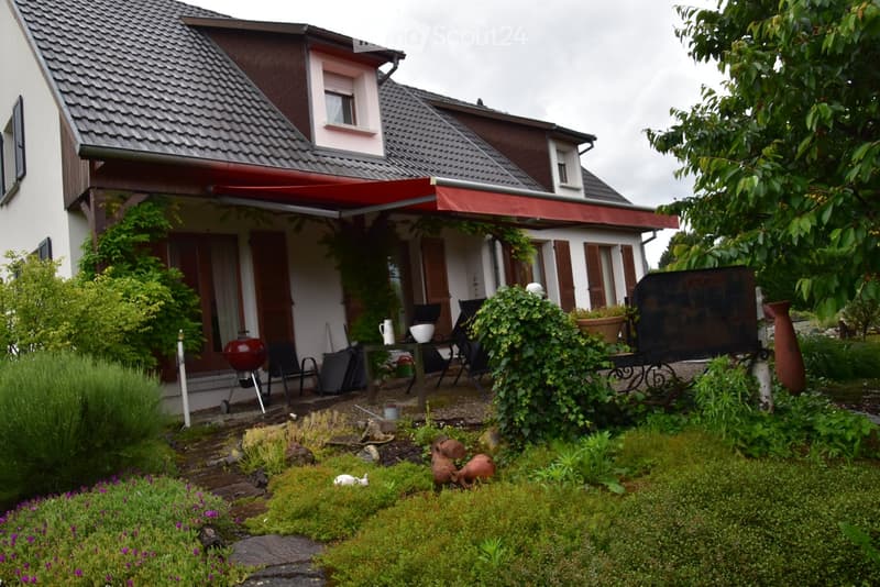 2-story house, red awning, outdoor table, chairs, barbecue, garden, shrubbery