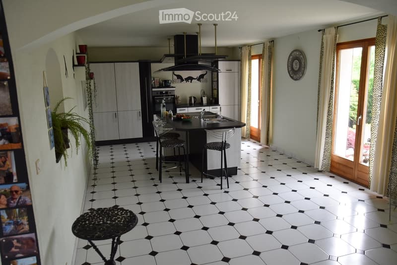 White and black tiled kitchen, kitchen island, stools, cabinets, open door to balcony, black range hood, counter, framed picture