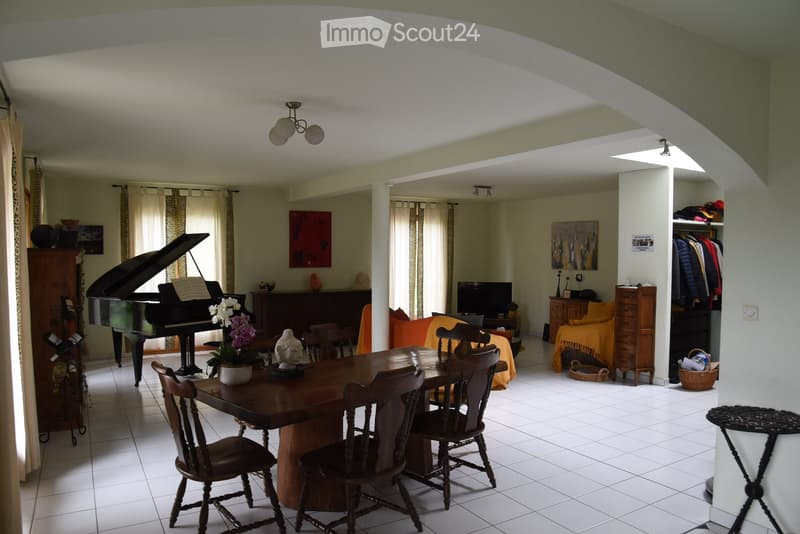 Dining area with a wooden table and chairs, black piano, television, cabinet, sofa, wooden flooring