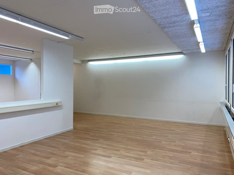 large room, hardwood floors, white walls, fluorescent ceiling lights, windows on two walls