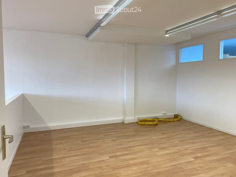 Empty room with white walls, wooden floor, windows, power outlets, and cables