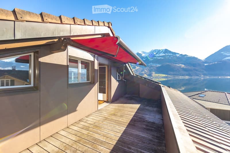 Exterior view of a building, wooden deck, retractable red awning, two windows with glass, overlooking a lake and mountains