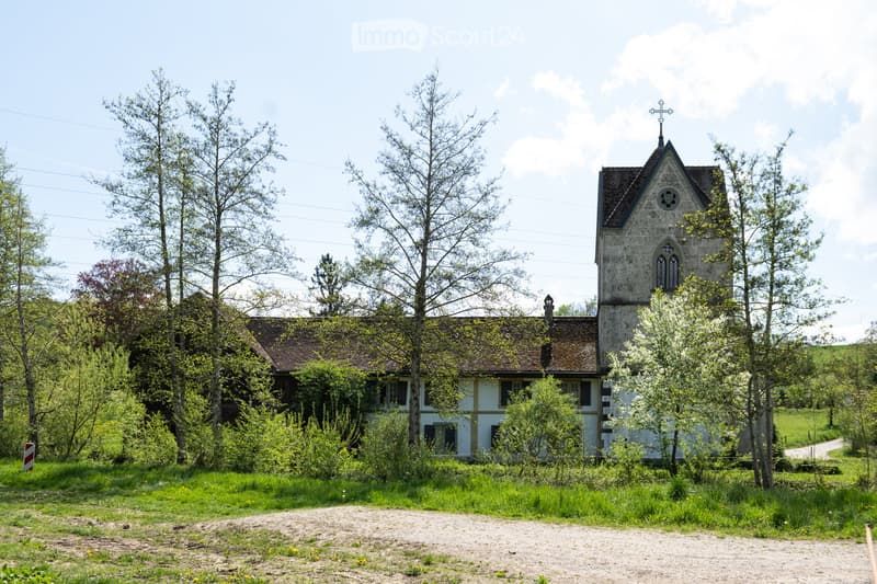 Old church with a tower, surrounded by trees and grass, located in a rural area