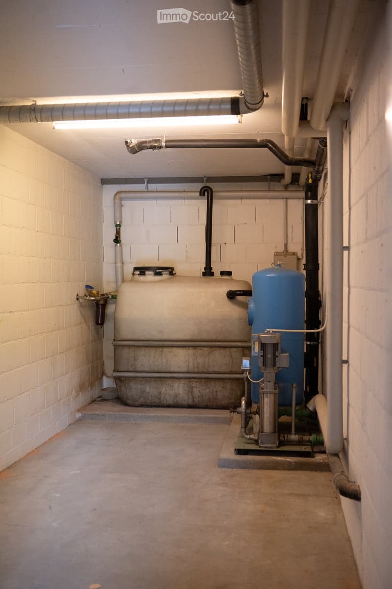 Utility room with white brick walls, concrete floor, large white and blue tanks, pipes, and a pump