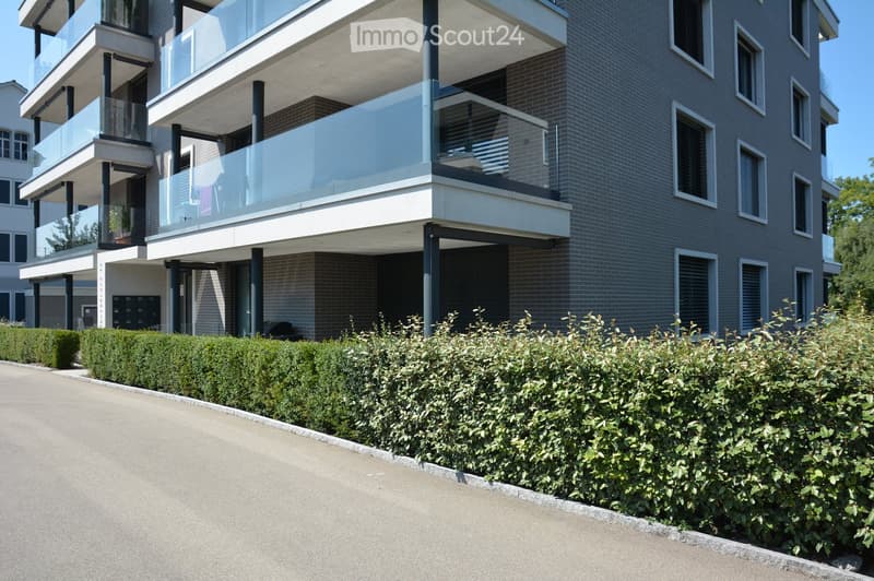 modern building with brick and glass facade, multiple terraces on different floors, shrubs in the front