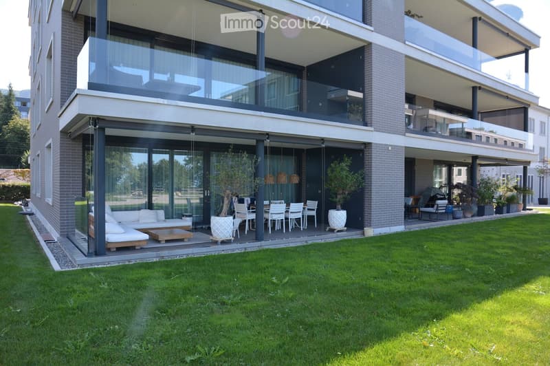 modern apartment building with glass walls, outdoor seating, glass doors, green lawn, potted plants