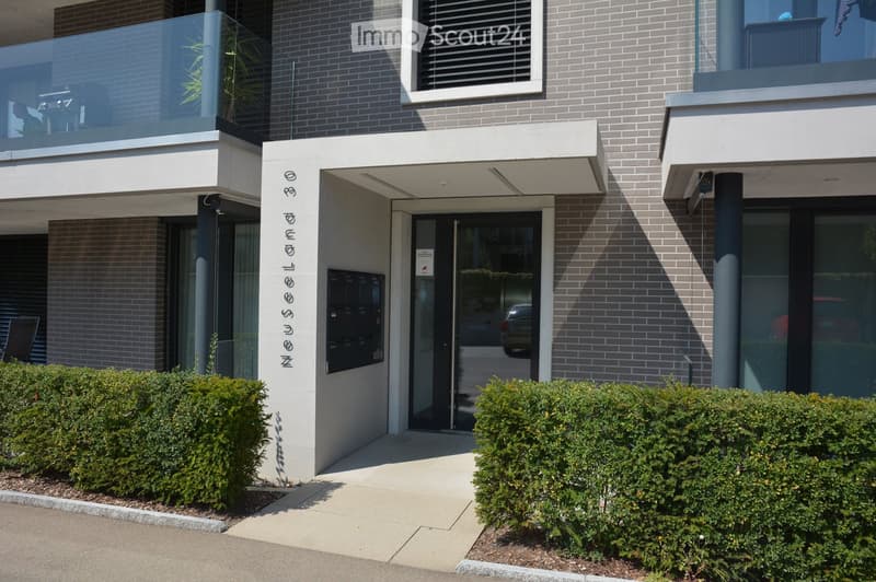 modern building with brick walls, glass doors, glass balcony, landscaped bushes, walkway, mailboxes